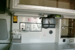 iInterior of an ambulance wall with medical equipment, including a no smoking sign, electrical outlets, a radio, and an oxygen gauge